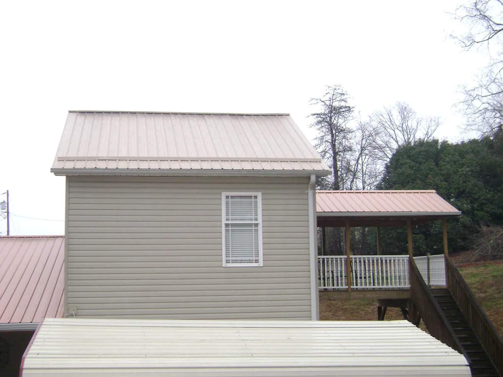 Tan metal roofs on a two story addition and attached porch, from a Roof Replacement job in Falmouth